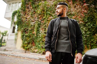 Tarz sahibi Arap sakallı adamın portresi gri balıkçı yaka ve siyah jaket giyiyor. Sonbahar yapraklarının arka planındaki Arap model adam..