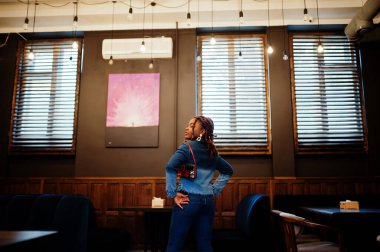 Cafe 'de mavi kot ceketli, siyah saçlı, Afro-Amerikan bir kadın. Güzel, havalı, modaya uygun, siyah, genç bir kız..