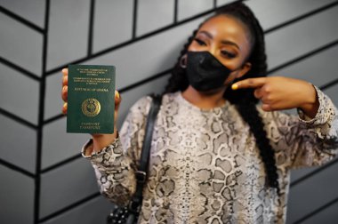 Siyah maskeli Afrikalı kadın elinde Gana pasaportu olduğunu gösteriyor. Afrika ülkesinde Coronavirus, sınır kapatma ve karantina, virüs salgını kavramı.