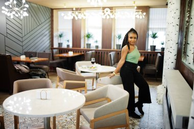 Restoranda yeşil kazak ve siyah kot pantolon giyen çekici Afro-Amerikan kadının portresi..