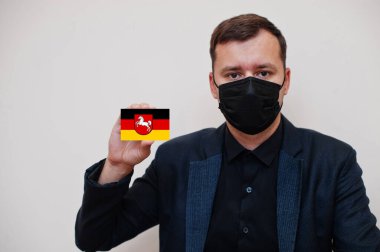 Alman adam siyah kıyafetler giyer ve yüz maskesini korur. Alt Saksonya bayrak kartını beyaz arka planda ayrı tutar. Almanya Coronavirus Covid kavramını açıkladı.