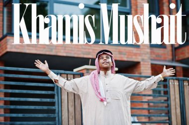 Khamis Mushait - biggest city of Saudi Arabia. Middle Eastern saudi arabian man posed on street against modern building up his hands in the air. clipart