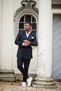 Genç ve yakışıklı Afro-Amerikan iş adamı portresi ve eski sütunun yanında beyaz spor ayakkabılar..