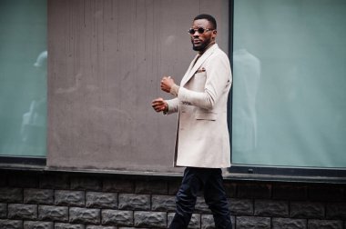 Afro-Amerikalı şık adam güneş gözlüklü bej ceket giyiyor..