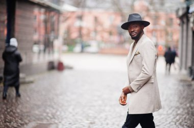 Afro-Amerikalı şık bir adam bej ceket ve siyah şapka giyer..