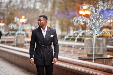 Genç ve yakışıklı Afro-Amerikan iş adamının portresi. Takım elbiseli, şehrin ortasında çelenklerle yürüyor..