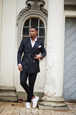 Genç ve yakışıklı Afro-Amerikan iş adamı portresi ve eski sütunun yanında beyaz spor ayakkabılar..