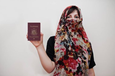Beyaz duvar arkasında Filipinler Cumhuriyeti pasaportu olan tesettür elbiseli genç Arap Müslüman kadın, stüdyo portresi. 