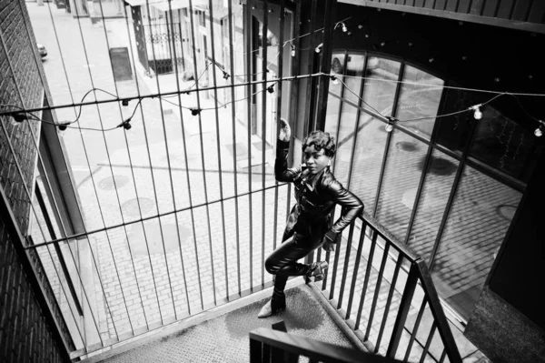 Fashionable beautiful african american woman posing in black leather jacket and pants at street.