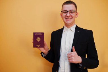 Fransız Cumhuriyeti pasaportunu sarı arka planda tutan yakışıklı genç adam, mutlu ve başparmağını kaldır. Avrupa ülke konseptine seyahat.