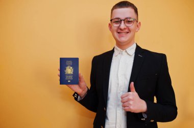 Sarı arka planda İzlanda pasaportu tutan yakışıklı genç adam, mutlu ve başparmağını kaldır. Avrupa ülke konseptine seyahat.