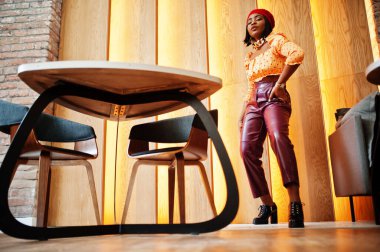 Kırmızı Fransız bereli zarif Afro-Amerikan kadın, büyük altın zincirli polka bluz ve deri pantolon, iç mekânda poz veriyor..