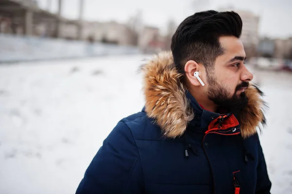Beard indian man wear jacket in cold winter day. Mobile earphones in ears.
