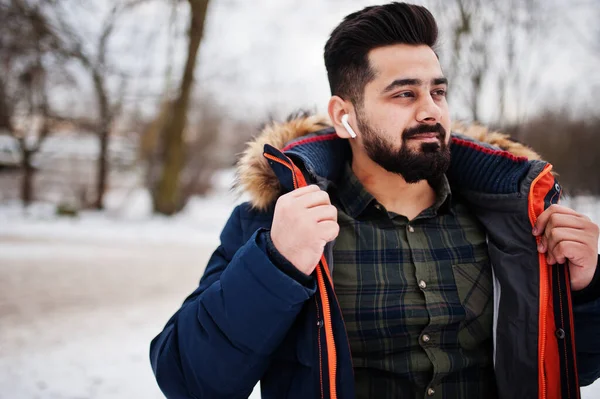 Beard indian man wear jacket in cold winter day. Mobile earphones in ears.