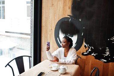 Kafedeki Afrikalı kadın bir fincan çayla cep telefonuna bakıyor..