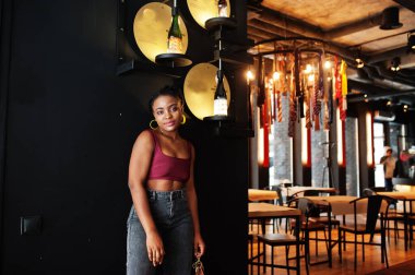 Kırmızı Marsala bluzlu ve kot pantolonlu Afrikalı kadın..