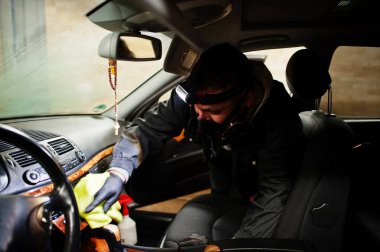 Üniformalı ve solunum cihazlı bir adam. Araba yıkama merkezinde çalışıyor. İçini sıcak buhar temizleyicisiyle temizliyor. Araba temizleme kavramı.