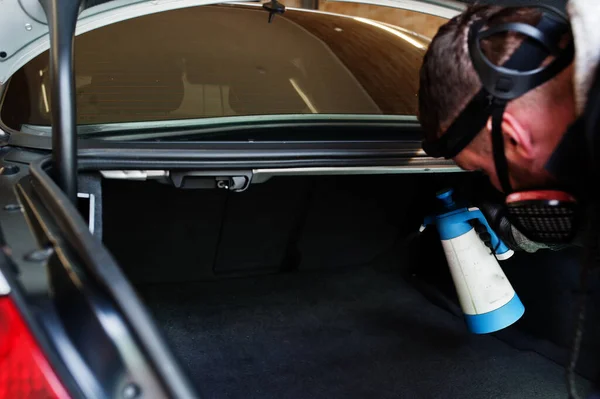 Man in uniform and respirator, worker of car wash center, cleaning car interior with hot steam cleaner. Car detailing concept.