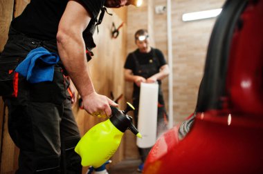 Araba servisi çalışanı, araba tamirhanesindeki kırmızı bir arabanın üzerine çakıl önleyici film koymuş. Özel filmli araba koruması.