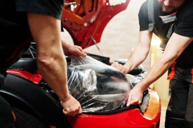 Araba servisi çalışanı, araba tamirhanesindeki kırmızı bir arabanın üzerine çakıl önleyici film koymuş. Özel filmli araba koruması.