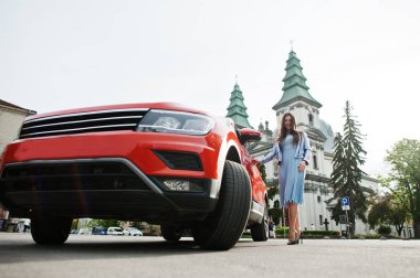 Turuncu SUV 'un yanında poz veren muhteşem bir kadının açık hava fotoğrafı..