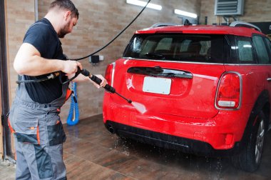 Garajda kırmızı araba yıkayan bir işçi..