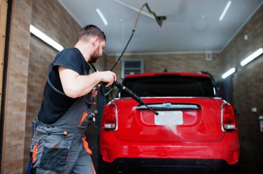 Garajda kırmızı araba yıkayan bir işçi..