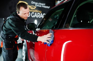 Garajda kırmızı araba yıkayan bir işçi..