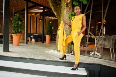 Hoş görünümlü, şık, çekici, hoş, içeriği hoş, neşeli, Afro-Amerikan kızının portresi parlak, parlak, parlak, sarı renkli bir ceket ya da kostüm giyer..