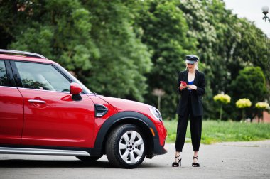 Şapkalı, siyah makyajlı, kırmızı şehir arabasının yanında, cep telefonlu güzel sarışın, seksi model portresi..