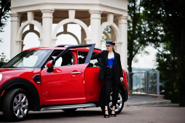 Şapkalı, siyah, mavi korseli, kırmızı şehir arabasının yanında parlak makyajlı güzel, sarışın, seksi kadın modelin portresi.. 