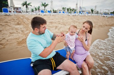 Yaz tatilleri. Ebeveynler ve insanlar çocuklarla birlikte dışarıda faaliyet gösteriyor. Mutlu aile tatilleri. Baba, hamile anne, bebek kız deniz kumsalında güneşleniyorlar.. 