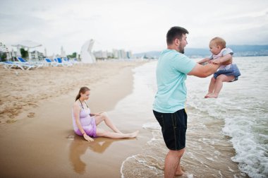 Yaz tatilleri. Ebeveynler ve insanlar çocuklarla birlikte dışarıda faaliyet gösteriyor. Mutlu aile tatilleri. Baba, hamile anne, küçük kız deniz kumsalında.. 