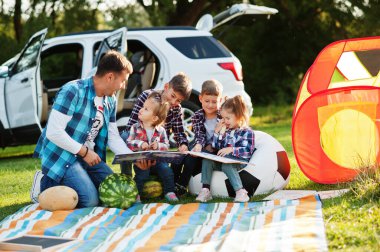 Aile birlikte vakit geçiriyor. Babam çocuklarla dışarıda arazi araçlarına karşı kitap okuyor..