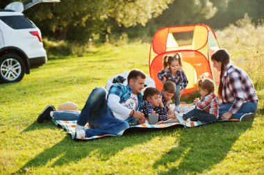 Aile birlikte vakit geçiriyor. Dışarıda piknik battaniyesi içinde dört çocuk ve aile. Kareli gömlekli büyük bir aile..