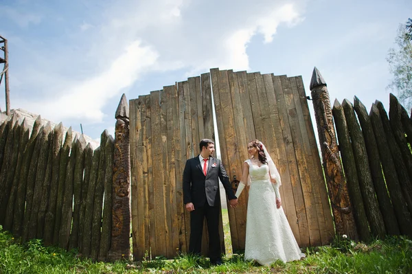 Весільна пара біля старого дерев'яного паркану тримає руки — стокове фото