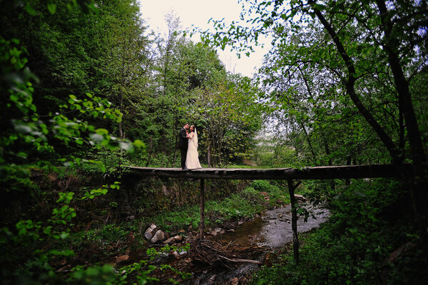 Wedding couple stay at the wooden bridge across mountain river
