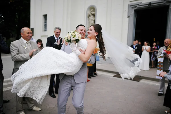 Marié heureux tenant sa mariée sur les mains près de l'église — Photo