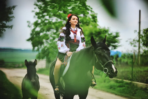 Young brunette girl on national dress with horses — Stock Photo, Image