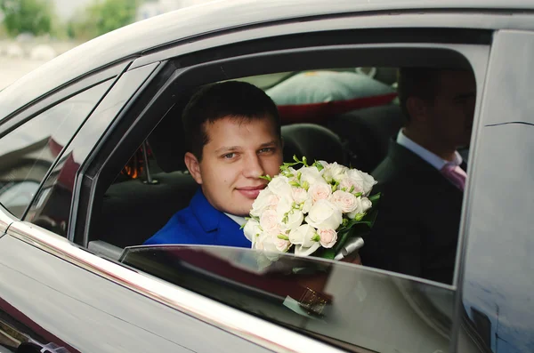Bruidegom met bruiloft boeket zittend op de auto — Stockfoto