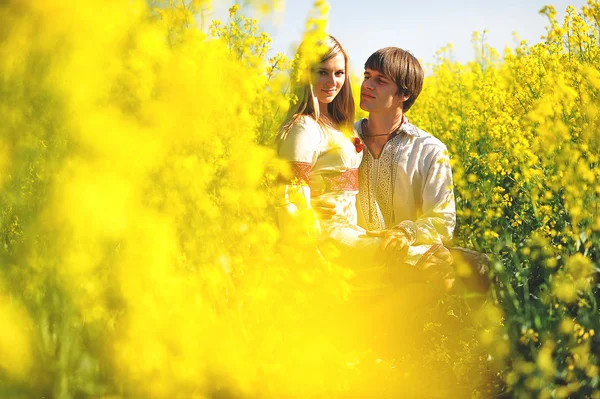 Couple on traditional dress at yellow flowers field — Stock Photo, Image