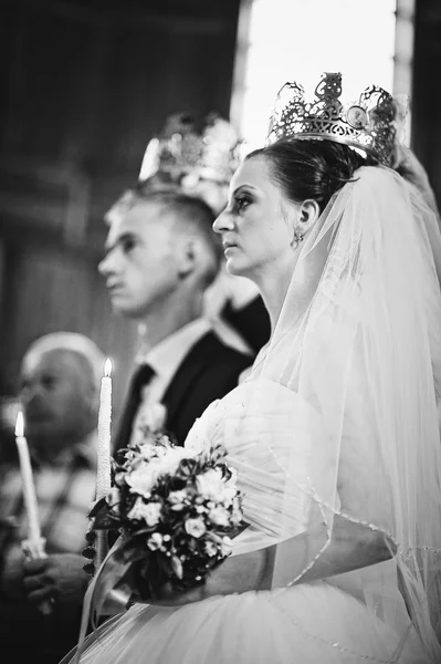 Wedding couple at the church with candles on hands and crown on — Stock Photo, Image