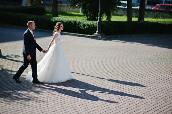 Mers pe jos ținându-se de mâini cuplu nunta și umbrele lor — Fotografie, imagine de stoc