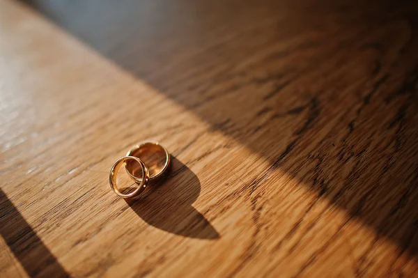 Two wedding rings in shadows on wooden table — Stock Photo, Image