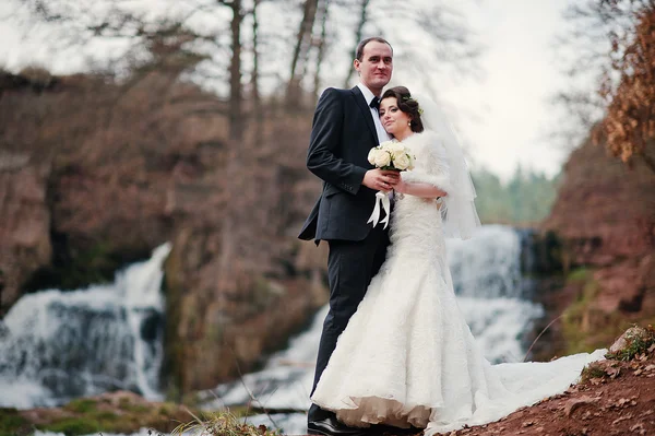 Lovely newlyweds background waterfall at cold autumn day — Stock Photo, Image