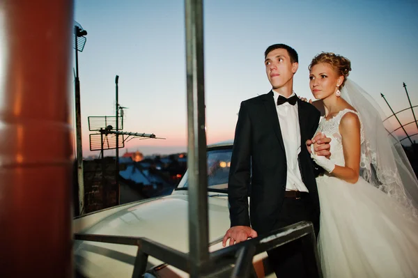 레트로 자동차와 함께 저녁에 건물의 지붕에 결혼식 한 쌍 — 스톡 사진