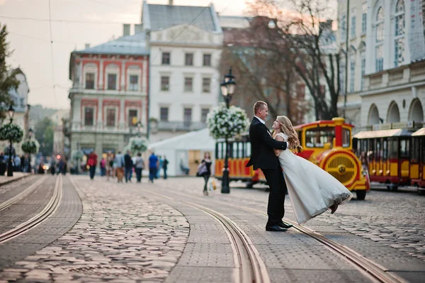 Bräutigam hält an der Hand Braut Hintergrund Stadt mit Kindern Zug — Stockfoto