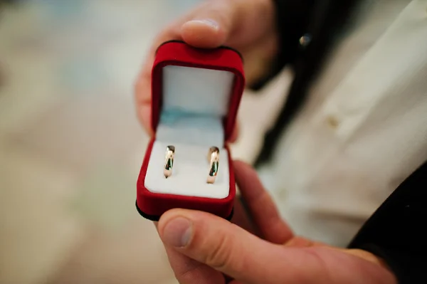 Anéis de casamento na mão do noivo na caixa de veludo vermelho — Fotografia de Stock