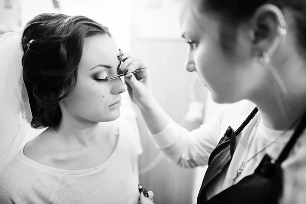 Hermosa joven novia sentada en la silla y maquillaje artista haciendo — Foto de Stock