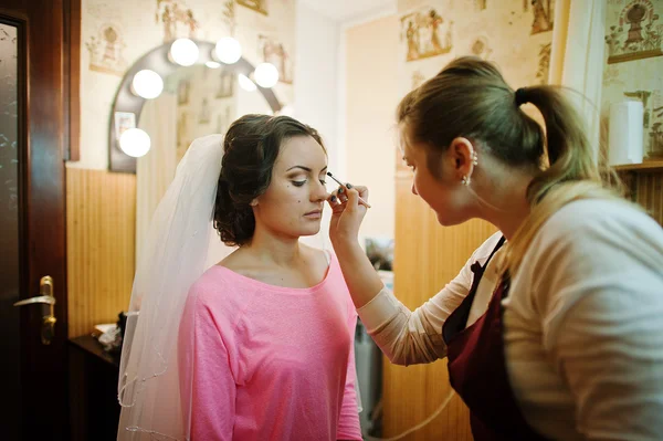 Linda jovem noiva sentada na cadeira e maquiagem artista fazendo — Fotografia de Stock